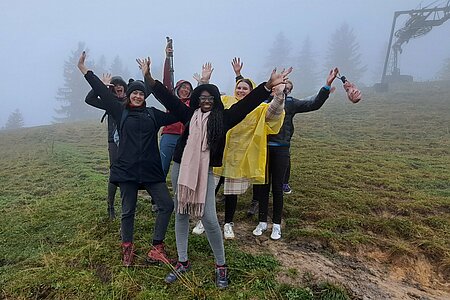 [Translate to English:] Gruppe steht mit Regenschirmen im Nebel auf dem Berg