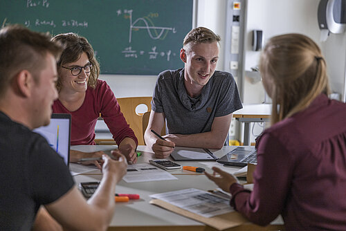 Vier Studierende sitzen an einem runden Tisch und arbeiten an einem Projekt