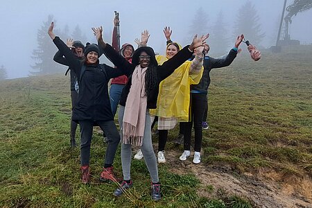 Group on the mountain with foggy wheather raising their arms.