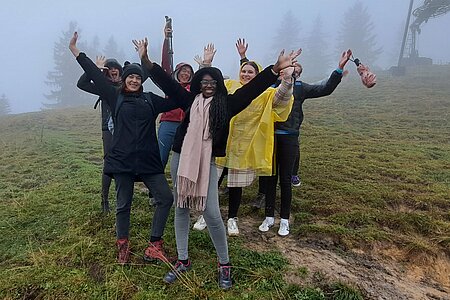 Gruppe steht im Nebel auf dem Berg und hebt die Arme