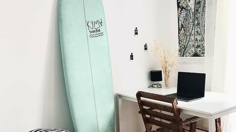 A student room, a surfboard leaning against the wall.