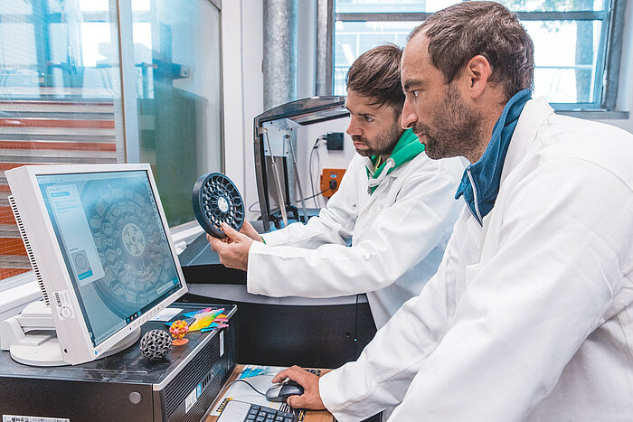 Das Bild zeigt zwei Personen, die im Labor für additive Fertigungsverfahren an der TH Rosenheim arbeiten. 