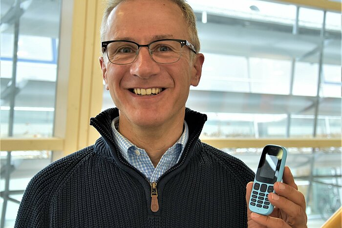 Auf diesem Portraitbild ist Prof. Dr.-Ing. Holger Stahl mit seinem Handy zu sehen.