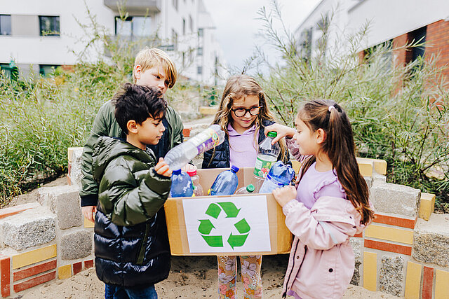Vier Kinder stehen um eine Kiste mit Recycling-Symbol