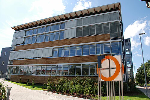 [Translate to English:] Außenansicht S-Bau am Campus Rosenheim mit Logo vor dem Gebäude