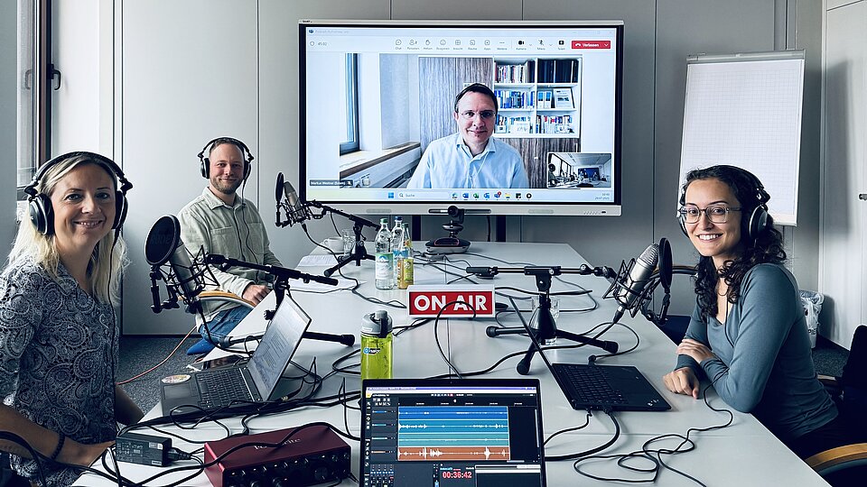 Drei Personen sitzen an einem Tisch und zeichnen einen Podcast auf.