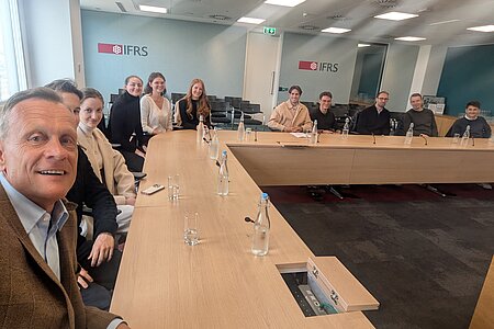 Prof. Dr. Bernd Hacker sitzt mit den Studierenden an einer langen Tafel bei IASB. Sie freuen sich auf den kommenden Vortrag.