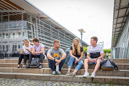 [Translate to English:] Gruppe Studierender am Campus Rosenheim sitzen auf Treppenstufen 