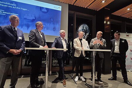 Man sieht alle sechs Sprecher des Abends auf dem Podium zur abschließenden Diskussionsrunde.