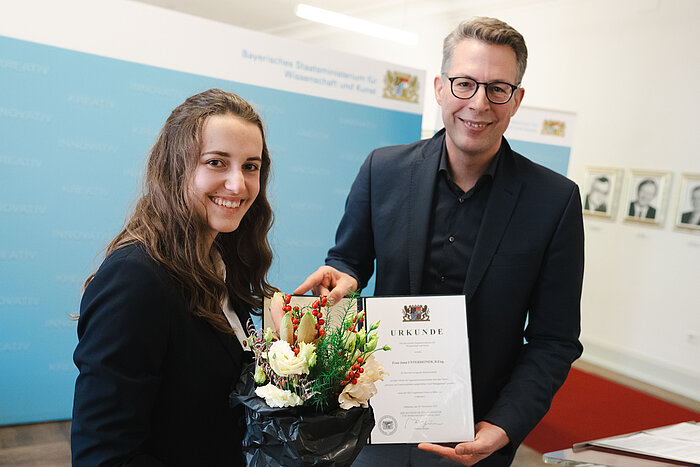 Das Bild zeigt die Absolventin Jana Unterreiner neben Wissenschaftsminister Markus Blume.