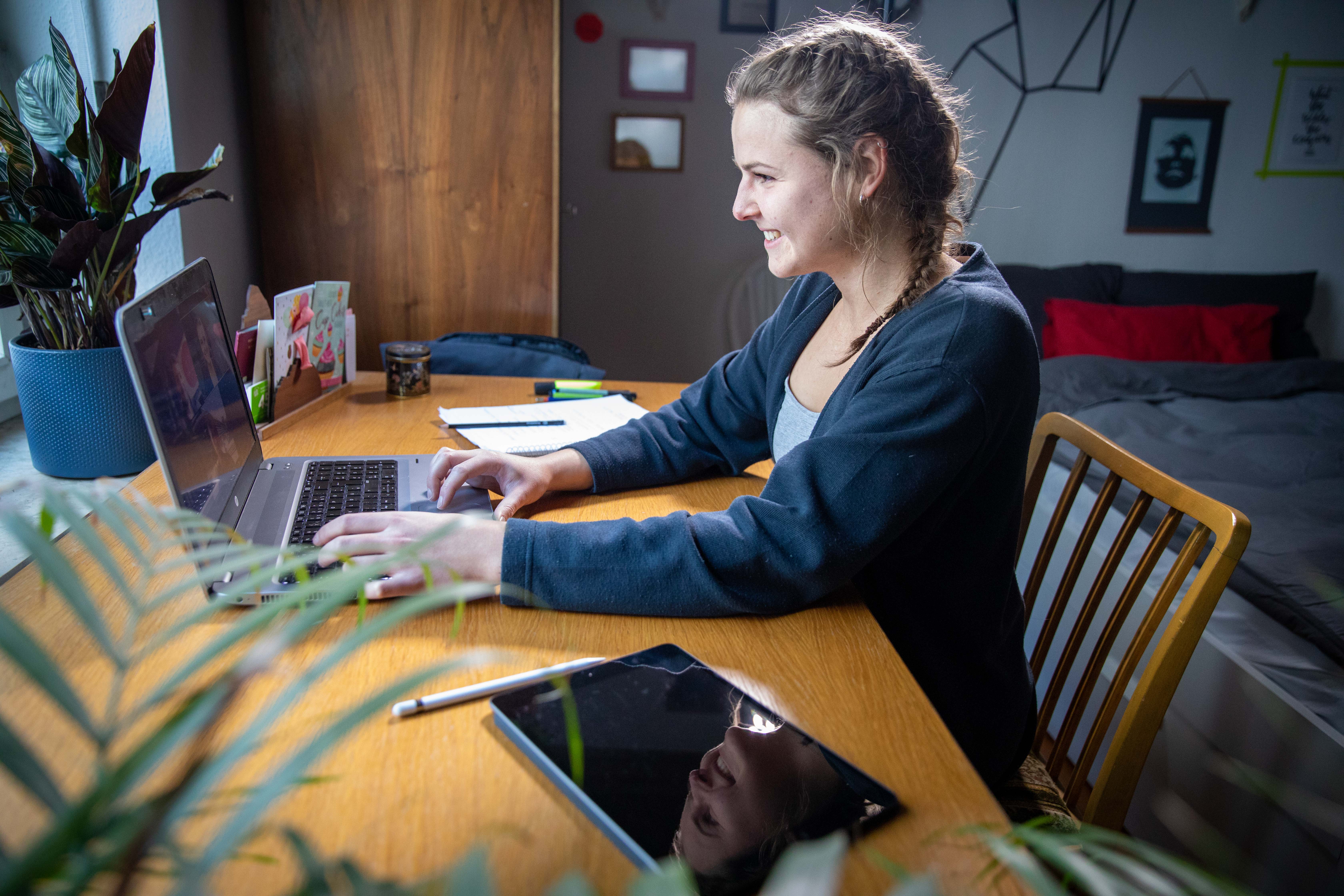 Studentin sitzt zu Hause am Schreibtisch und arbeitet am Laptop